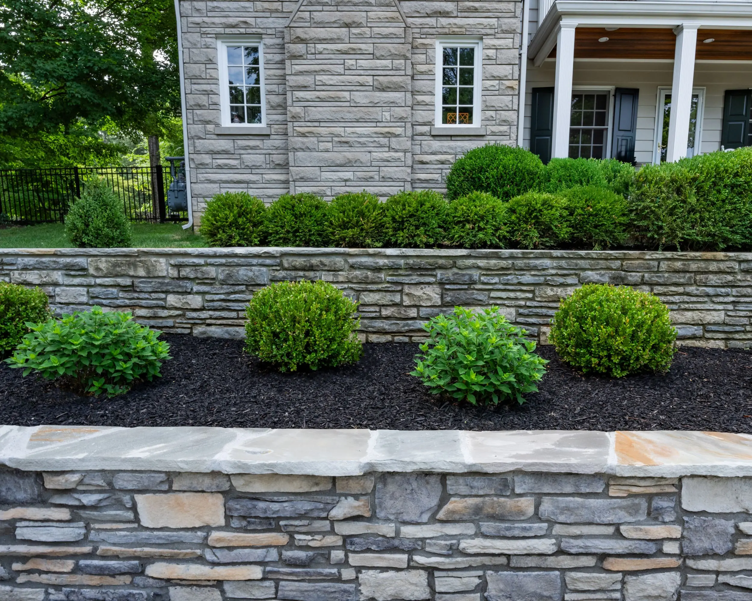 a well landscaped backyard in Louisville, kentucky shows multiple retaining walls with several species of bushes and black mulching.