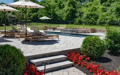 Landscape & Horticultural Services A beautiful backyard landscape with horticultural services in Louisville features a stone patio with lounge chairs and umbrellas beside a small pool.